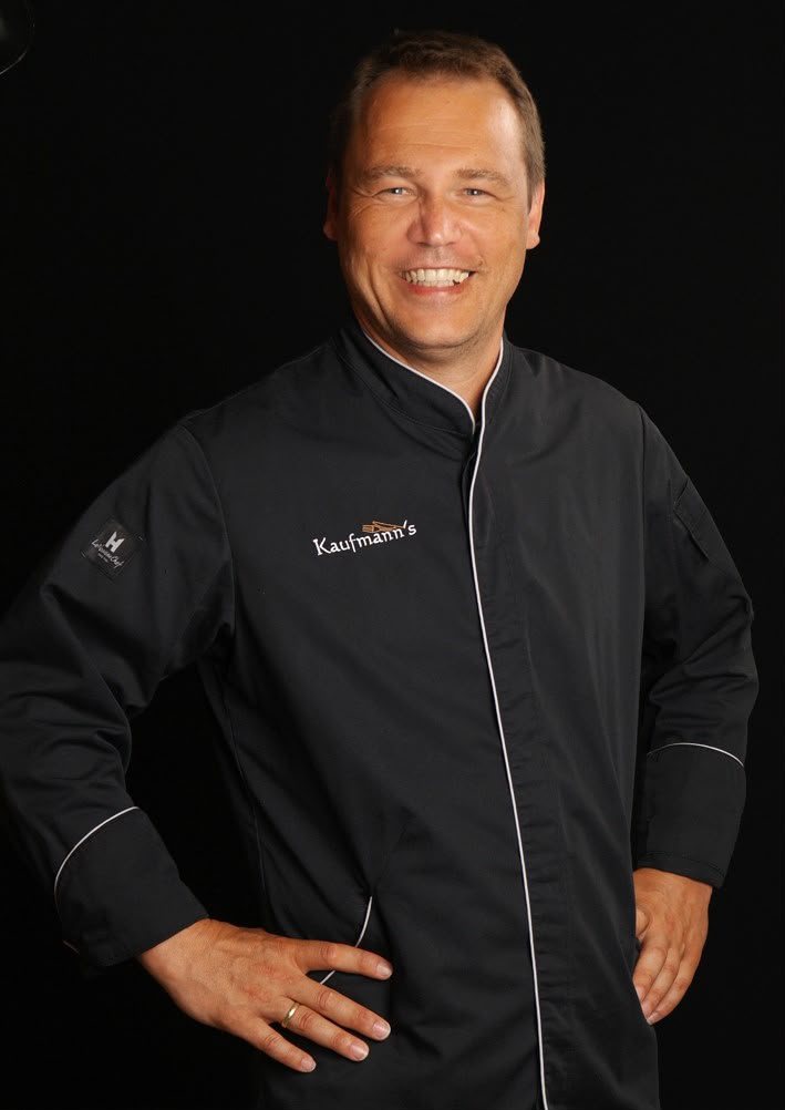 Joachim Kaufmann in schwarzer Kochjacke, lächelnd, die Hände in den Hüften